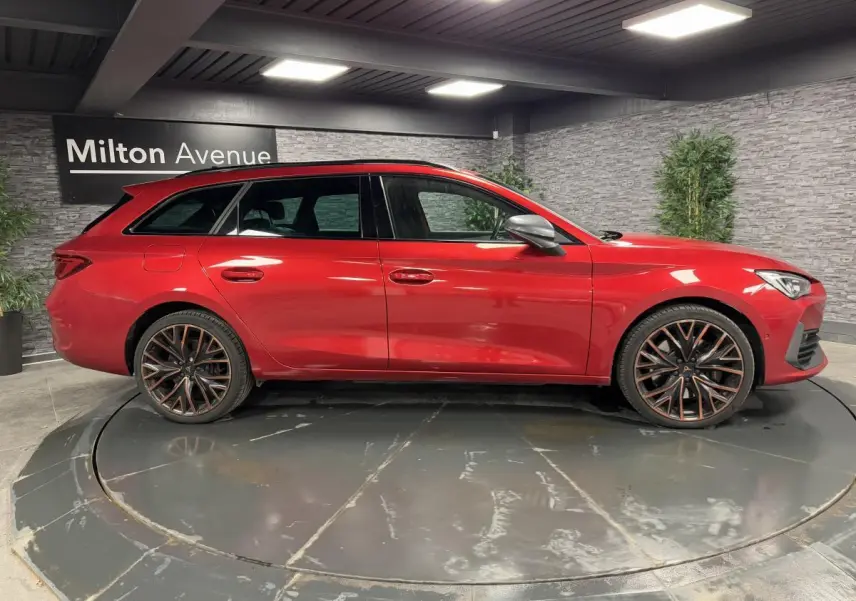 Profil droit d'une CUPRA Leon Sportstourer rouge Désir avec jantes alliage 19 pouces Palm Springs en intérieur showroom.