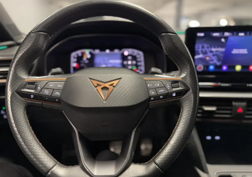 Volant en cuir perforé avec logo CUPRA cuivré, vue frontale sur le tableau de bord numérique et écran tactile du Leon Sportstourer rouge.