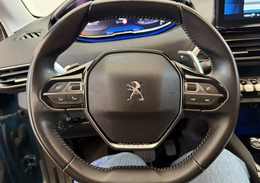 Vue rapprochée du volant cuir noir du Peugeot 3008 2021 avec tableau de bord numérique et écran tactile visible en arrière-plan.