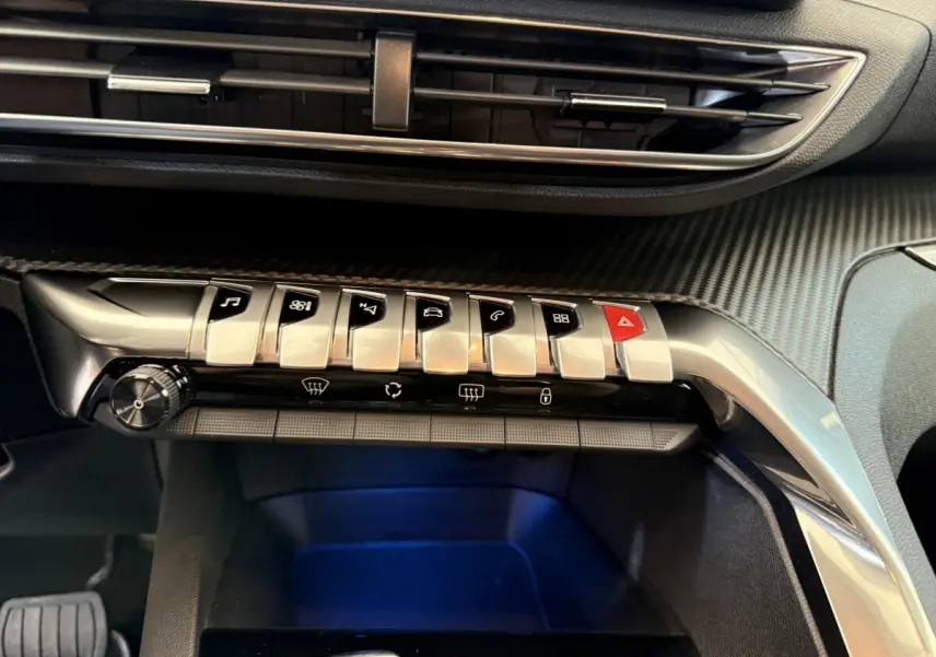 Gros plan sur la console centrale du Peugeot 3008 bleu, mettant en valeur les boutons de commande en métal et le revêtement carbone.