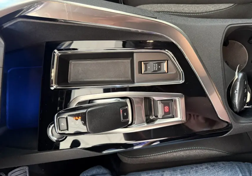 Gros plan sur la console centrale noire brillante du Peugeot 3008 bleu, avec levier de vitesse automatique et bouton frein à main électrique.