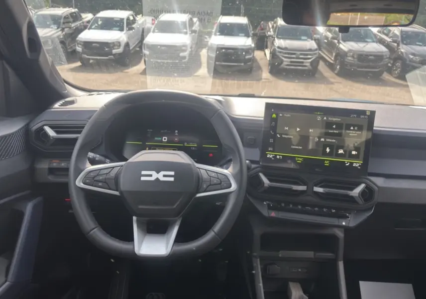 Vue intérieure du tableau de bord du Dacia Bigster Hybrid-G 150, avec volant cuir et écran tactile central allumé.