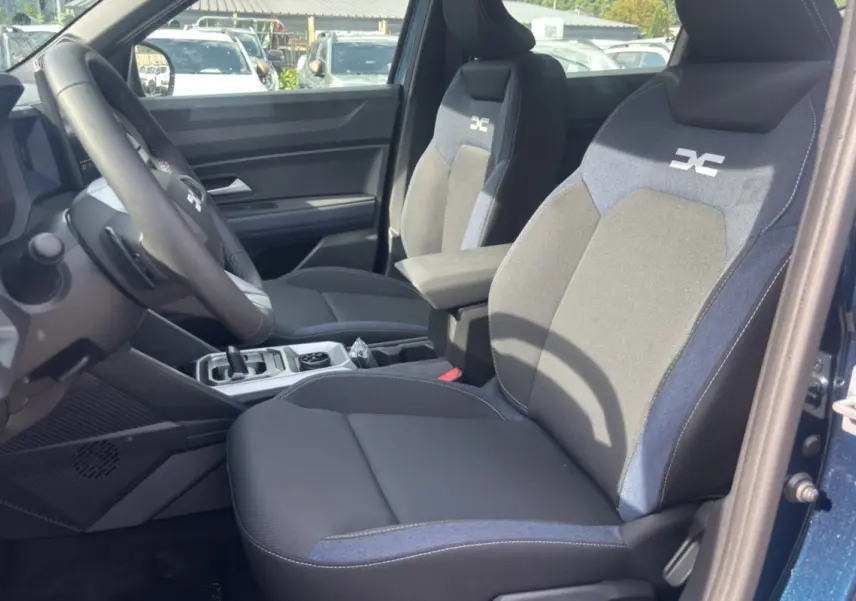 Vue intérieure côté conducteur du Dacia Bigster bleu indigo, mettant en valeur les sièges tissu bicolores avec logo brodé.