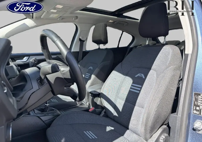 Vue intérieure côté conducteur de la Ford Focus 1.0 Flexifuel 2022, sièges tissu noir avec toit panoramique bleu azur visible.