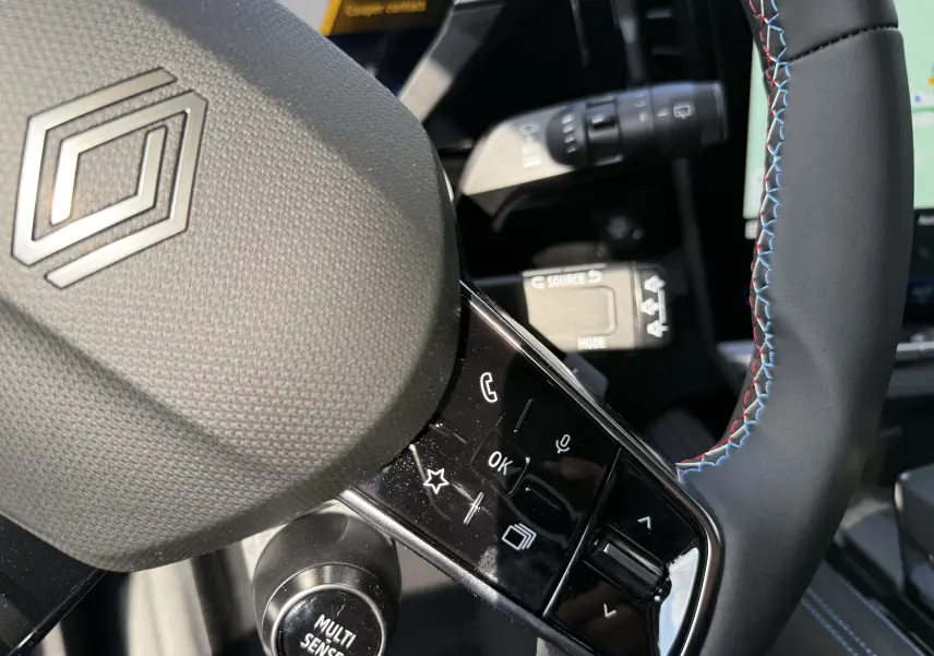 Gros plan sur le volant noir du Renault Espace 2025, avec surpiqûres tricolores et commandes intégrées.