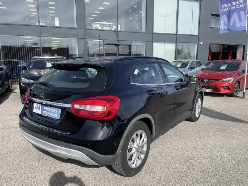 Mercedes GLA 200 D Sensation noir vue 3/4 arrière droit, stationné devant un showroom de véhicules d'occasion.