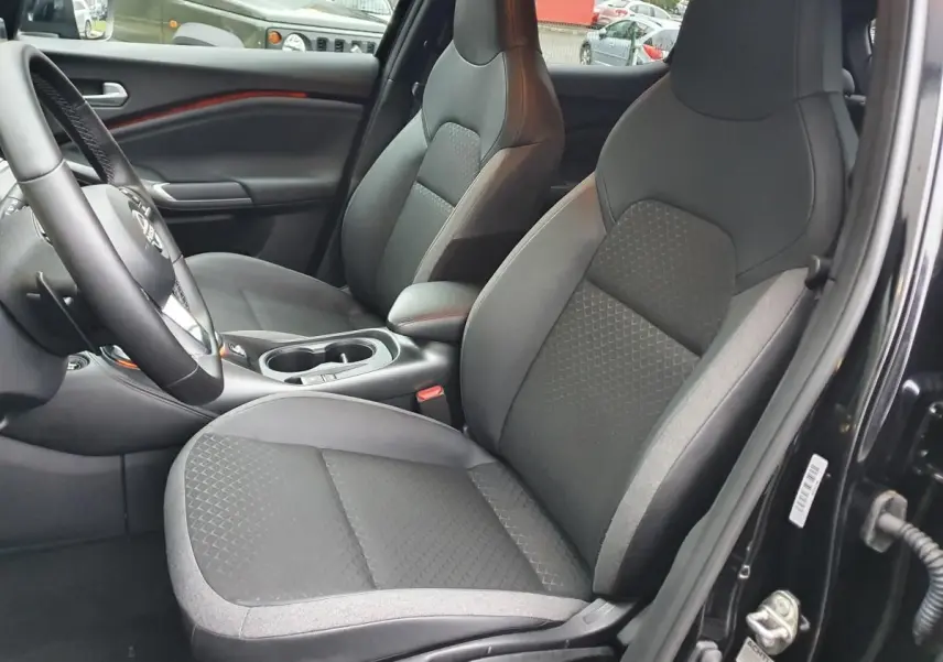 Intérieur côté conducteur du Nissan Juke noir 2025, sièges tissu gris avec console centrale et porte-gobelets visibles.