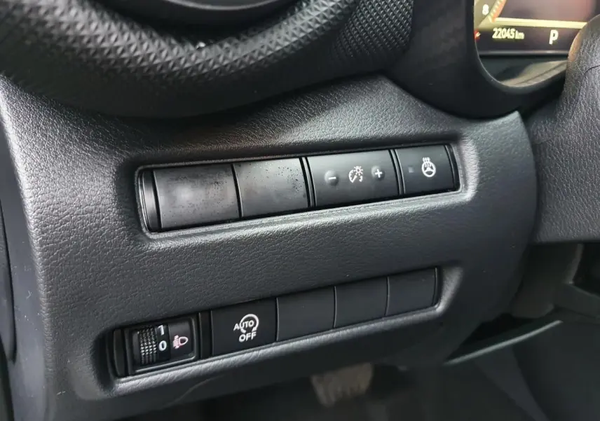 Gros plan sur les commandes de réglage d'éclairage et chauffage du volant côté gauche du tableau de bord du Nissan Juke noir 2025.