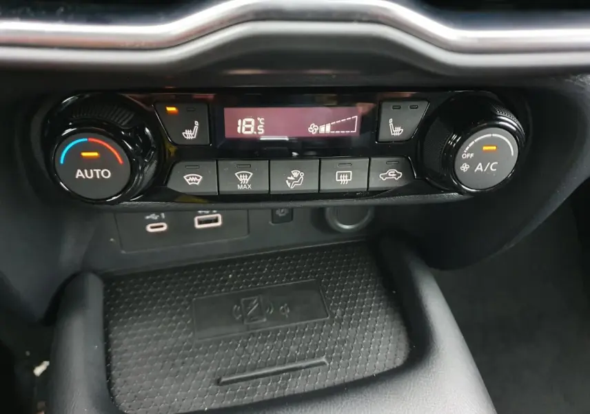 Vue rapprochée de la console centrale du Nissan Juke noire 2025, mettant en valeur la climatisation automatique et le chargeur sans fil.