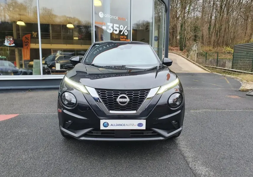 Vue avant d'un Nissan Juke noir 2025 avec phares LED allumés et calandre en V chromée.