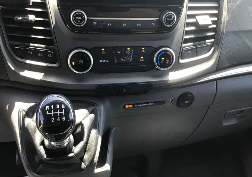 Gros plan sur la console centrale du Ford Transit Custom Kombi 2023, montrant le levier de vitesse manuel et les commandes de climatisation.