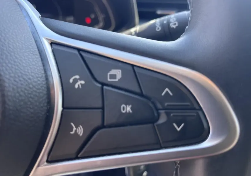 Gros plan sur les commandes multifonctions noires du volant de la Renault Clio 1.6 E-Tech blanc Quartz, version 2021.