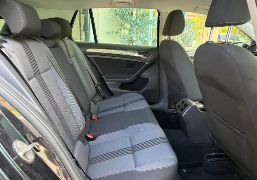 Vue intérieure côté gauche des sièges arrière d'une Volkswagen Golf 7 noire, tissu gris à rayures, avec porte ouverte.