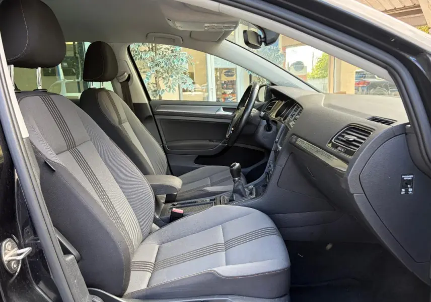 Intérieur côté conducteur de la Volkswagen Golf 7 noire, montrant sièges tissu, volant cuir multifonctions et boîte manuelle.