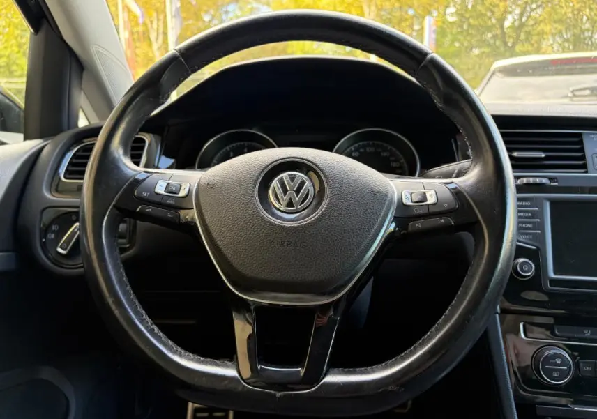 Vue rapprochée du volant cuir multifonctions noir d’une Volkswagen Golf 7, avec tableau de bord et console centrale visibles.