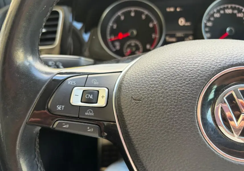 Gros plan sur le volant cuir noir multifonctions d’une Volkswagen Golf 7 avec commandes de régulateur de vitesse.