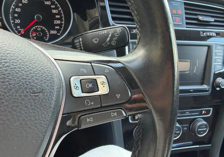 Gros plan sur le volant cuir multifonctions côté gauche d’une Volkswagen Golf 7 noire avec tableau de bord et commandes visibles.