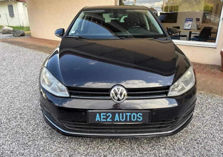 Vue frontale d'une Volkswagen Golf 7 noire, avec calandre et logo VW bien visibles sur un sol gravillonné.