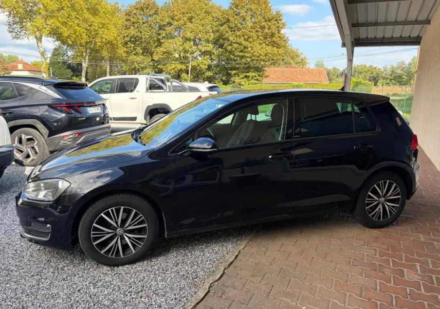 Volkswagen Golf 7 noire vue de profil côté gauche, stationnée sous abri avec jantes alliage distinctives.