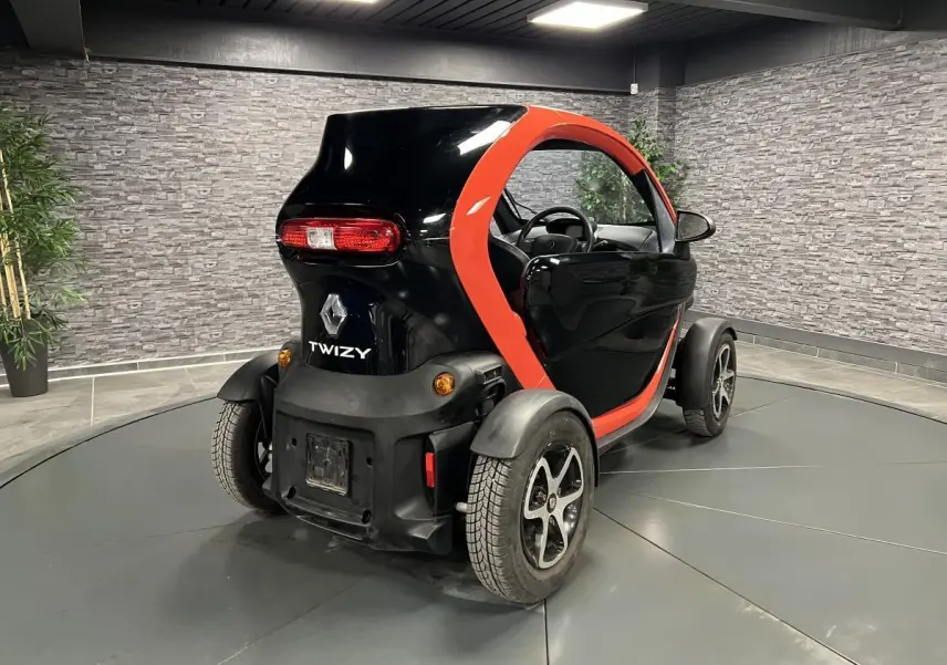 Vue 3/4 arrière droite d'une Renault Twizy orange et noire avec portes élytre dans un showroom intérieur.