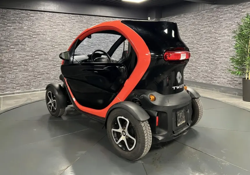 Vue 3/4 arrière droite d'une Renault Twizy Intens 2019 orange et noire avec portes élytre dans un showroom.