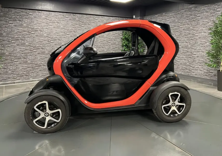 Profil côté gauche de la Renault Twizy Intens 2019 orange et noire, avec portes élytre dans un showroom.