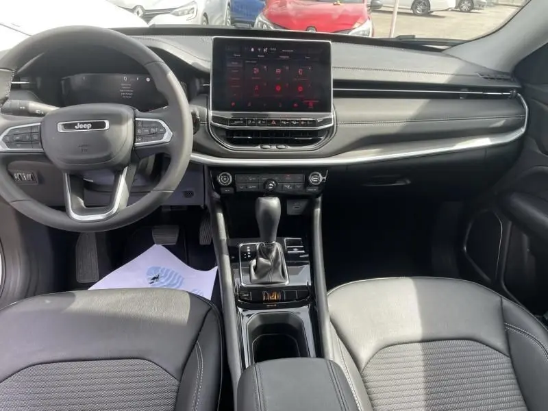 Vue intérieure avant du Jeep Compass 2024 blanc, avec tableau de bord moderne et écran tactile central lumineux.