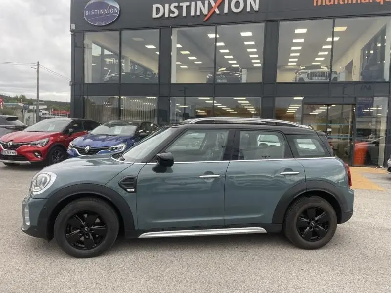 Vue de profil côté gauche d'un MINI Countryman Cooper 136 gris avec jantes noires, devant un concessionnaire Distinxion.