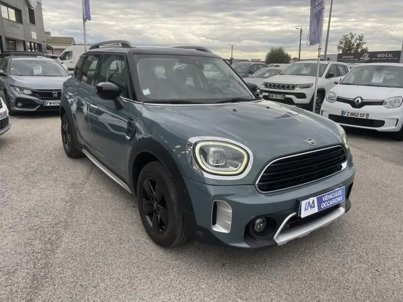 Vue 3/4 avant droite d'un MINI Countryman Cooper 136 gris avec jantes noires, sur un parking extérieur de concession.