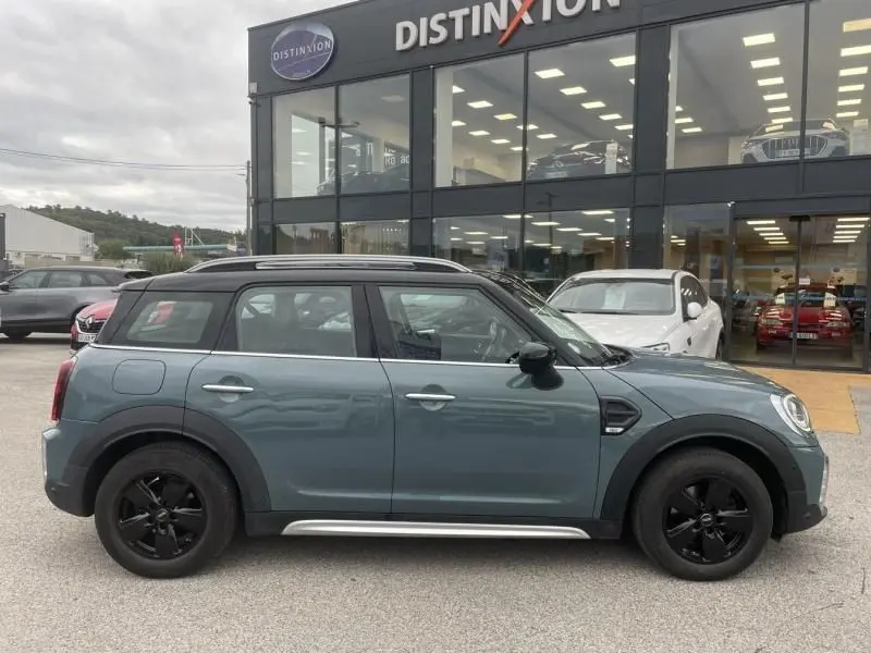 Vue latérale gauche d'une MINI Countryman Cooper 136 gris 2021 avec jantes noires, stationnée devant un concessionnaire Distinxion.