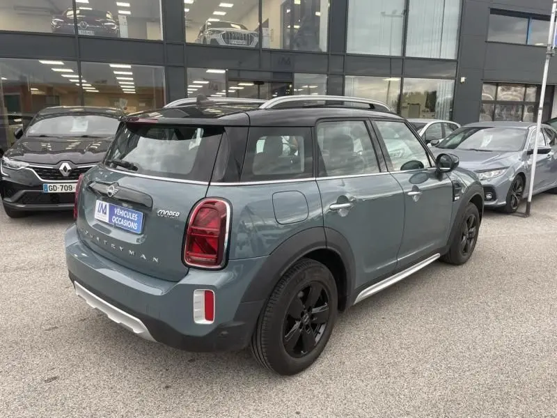 Vue 3/4 arrière droite d'une MINI Countryman Cooper 136 gris avec toit noir et jantes noires, stationnée devant un showroom.