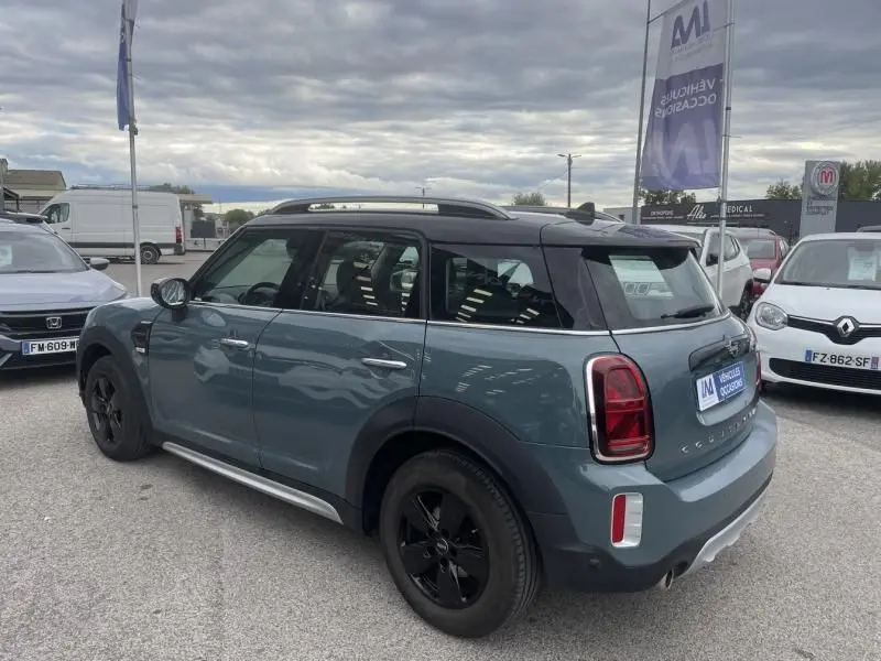 Vue 3/4 arrière côté gauche d'une MINI Countryman Cooper 136 gris 2021 avec toit noir et jantes noires sur parking.