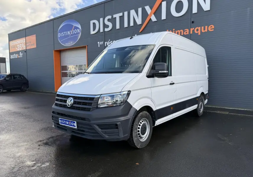 Volkswagen Crafter fourgon blanc vu en 3/4 avant droit devant un bâtiment gris avec logo Distinxion.