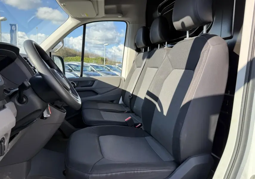 Vue intérieure côté conducteur du Volkswagen Crafter blanc, montrant les sièges avant en tissu gris et le volant multifonctions.