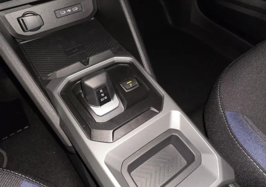 Vue rapprochée de la console centrale grise et noire du Dacia Duster 1.6 Hybrid 2025 avec levier de vitesses automatique et siège tissu Denim bleu.
