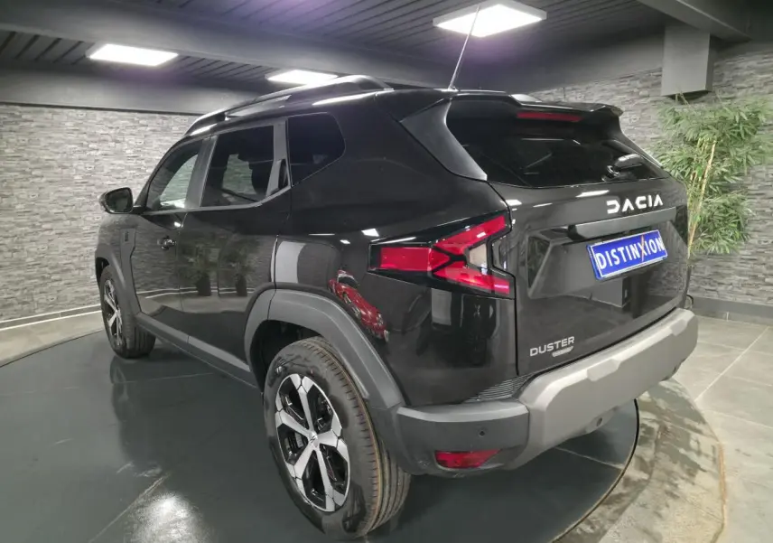 Vue 3/4 arrière droit du Dacia Duster 1.6 Hybrid noir nacré avec jantes alliage 18 pouces et barres de toit noires.