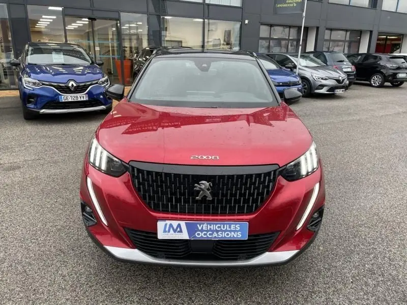 Vue avant d’un Peugeot 2008 rouge métal 2022 avec calandre noire et feux LED verticaux, sur parking de véhicules d’occasion.