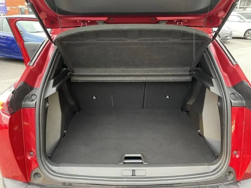 Coffre ouvert vu de l’arrière d’un Peugeot 2008 130 GT-LINE rouge métal de 2022, montrant un espace de chargement vide.