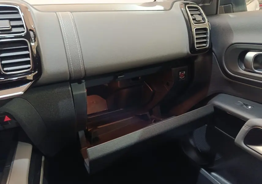 Vue intérieure côté passager du tableau de bord gris et noir avec boîte à gants ouverte du Citroën C5 Aircross Hybrid blanc.