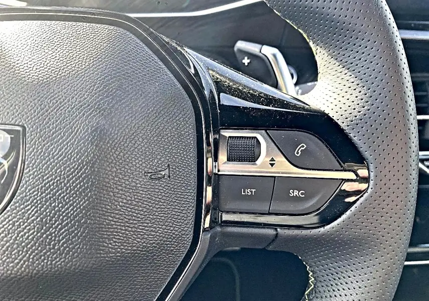 Gros plan sur le volant cuir perforé du Peugeot 2008 1.2 hybrid 145 GT, avec commandes multifonctions et palettes au volant.