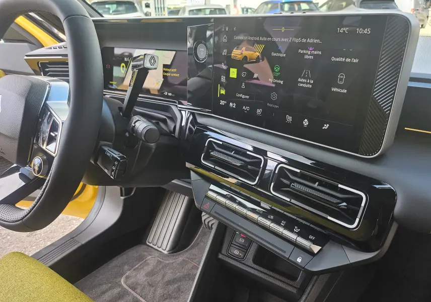 Vue intérieure côté conducteur de la Renault R5 Iconic 150 électrique jaune pop, avec tableau de bord numérique et écran tactile central.