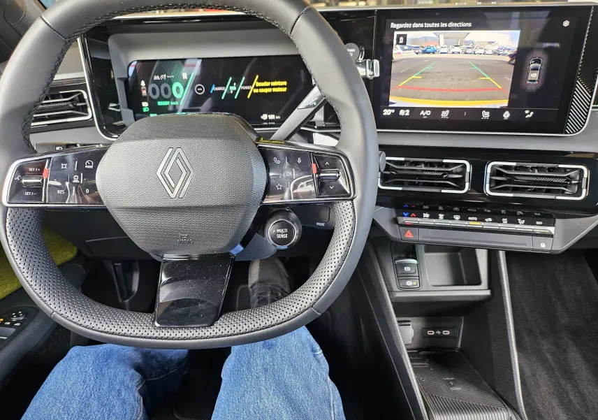 Vue intérieure centrée sur le volant Renault R5 électrique 2025, avec tableau de bord numérique et écran multimédia affichant la caméra de recul.