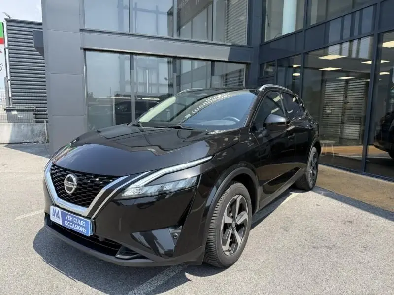 Nissan Qashqai noir 2023 en 3/4 avant droit, avec calandre chromée et phares LED fins, stationné devant un bâtiment vitré.