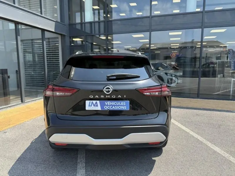 Vue arrière d'un Nissan Qashqai noir 2023 avec logo et plaque "Véhicules Occasions" sur parking devant vitrine.