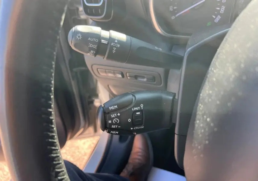 Gros plan sur les commandes de régulateur de vitesse et éclairage à gauche du volant d'une Citroën C3 Aircross beige.