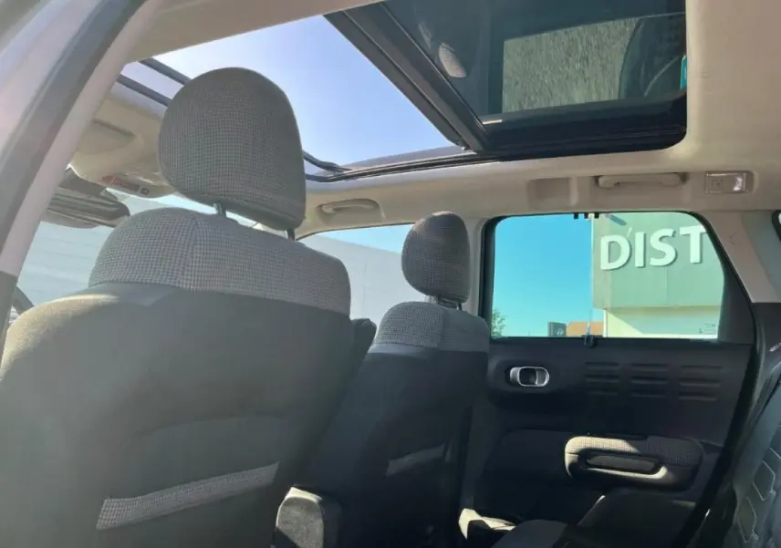 Vue intérieure arrière du Citroën C3 Aircross beige, mettant en valeur le toit ouvrant panoramique et les sièges en tissu et cuir noir.