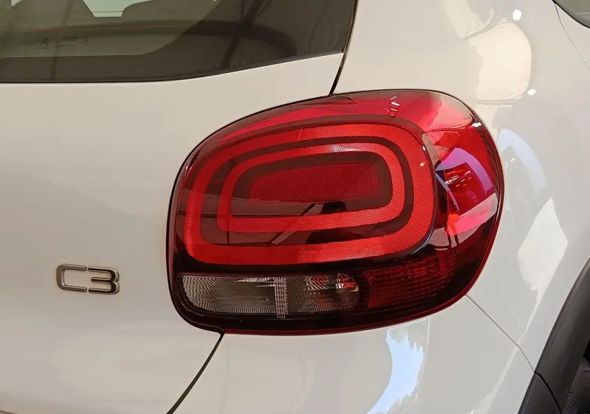 Gros plan sur le feu arrière droit rouge et le logo C3 d'une Citroën C3 blanche vue de l'arrière.