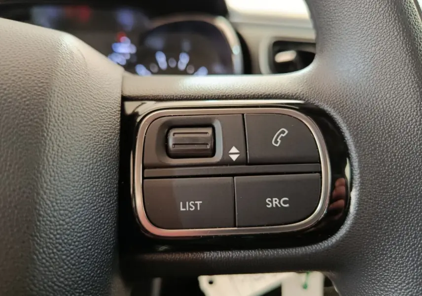 Gros plan sur les commandes gauche du volant noir de la Citroën C3 blanche, boutons pour téléphone et liste audio.