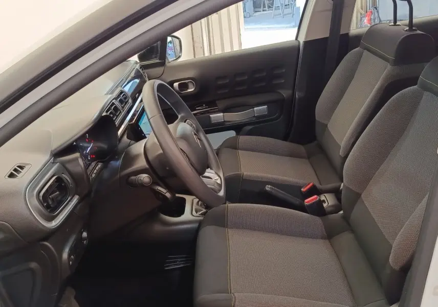 Intérieur avant de la Citroën C3 blanche 2020, vue côté conducteur montrant sièges et tableau de bord moderne.
