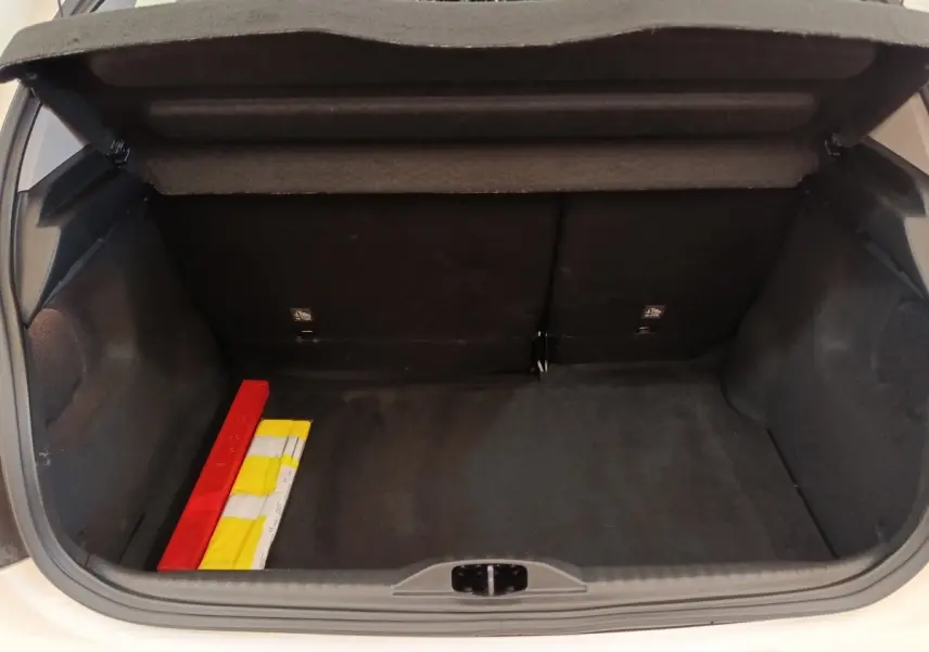 Coffre ouvert d’une Citroën C3 blanche, vue arrière, montrant un espace de rangement avec triangle de sécurité et gilet jaune.